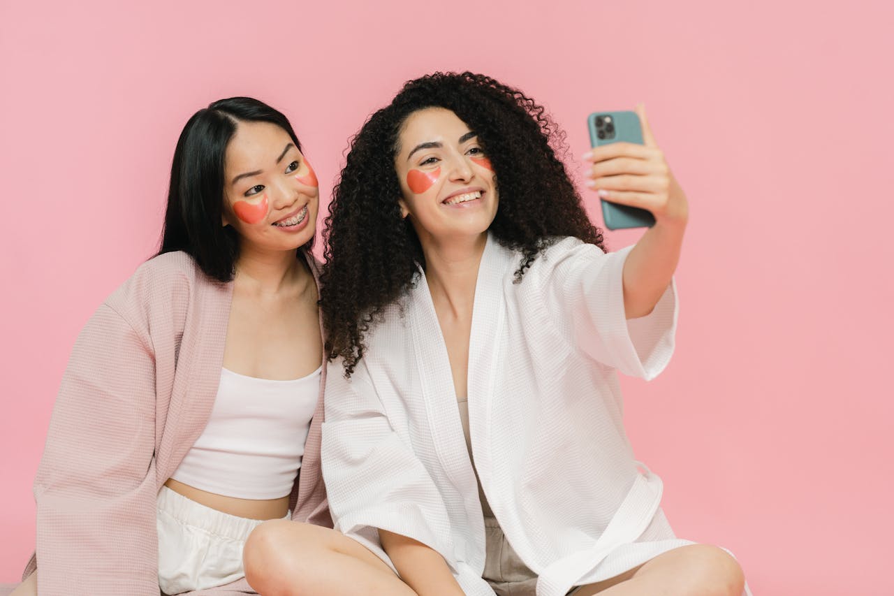 Two women in face masks and bathrobes enjoying a fun selfie session.